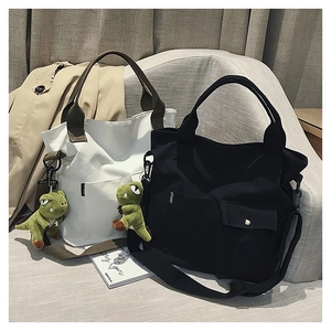 Detail view of canvas tote bags in cream and black featuring front pockets and sport labels