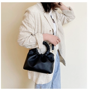 Detail view of a black pleated cloud handbag featuring unique ruched round handle and metal feet