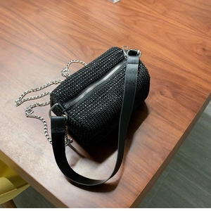 Gros plan du sac cylindrique noir orné de strass avec chaîne et poignée en cuir