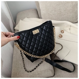 Detail of black quilted bucket bag with gold chain strap on a white wool coat