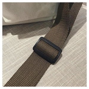 Close-up of adjustable brown woven shoulder strap with black buckle on canvas tote bag