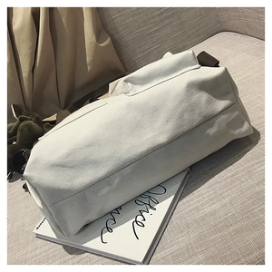 Detail of off-white canvas tote bag featuring brown shoulder straps and side flap pocket
