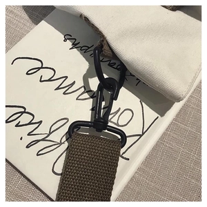 Detail of matte black metal swivel hook and brown strap on a white canvas tote bag