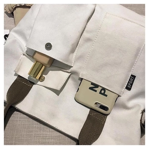 Detail of white canvas tote bag with functional utility pockets and green woven strap