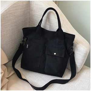 Detail of black canvas tote bag with front pockets and adjustable strap on a gray sofa