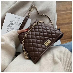 Macro detail of the dark brown quilted leather texture and gold metal turn-lock on the bag