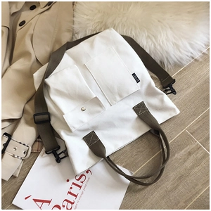 Detail of white canvas tote bag with olive green straps and functional front pockets