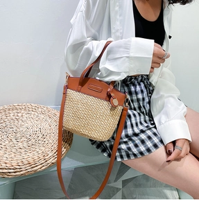 Detail of hand-woven straw tote with brown leather handles and a round metal charm