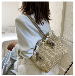 Detail of straw tote bag featuring thick rope handles, tassel decor, and floral lining