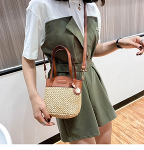 Detail of hand-woven straw bucket bag with brown leather handles and adjustable strap