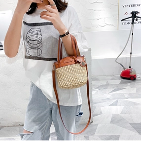 Detail of hand-woven straw bucket bag with brown leather handles and adjustable shoulder strap