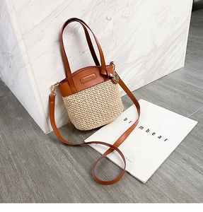 Detail of straw woven bucket bag with brown leather trim and adjustable shoulder strap