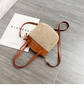 Detail of straw bucket bag with brown leather trim and dual straps on stone background