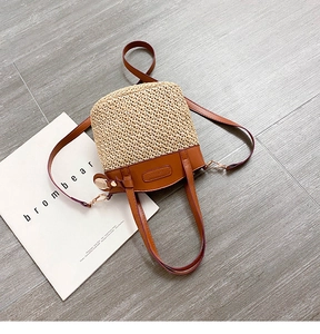 Detailed close-up of woven straw bucket bag with brown leather handles and stitching