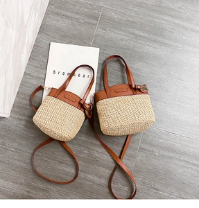 Top view of two beige straw bucket bags with brown leather handles and straps