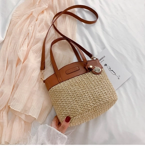 Detail of straw bucket bag with leather handle and adjustable shoulder strap on white linen