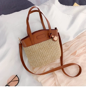 Close-up of straw bucket bag with brown leather trim and golden circular hardware