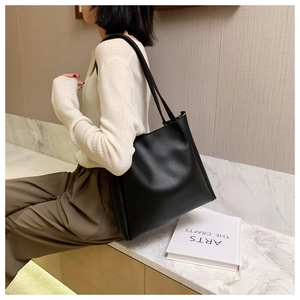 Detailed side view of a large black matte tote bag worn by a model in a minimal setting