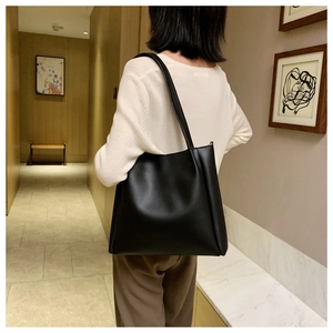 Minimalist black leather tote bag shown on a model in a stylish indoor corridor setting