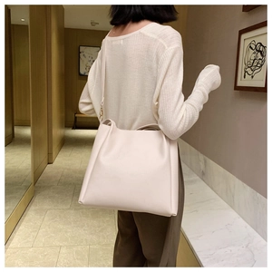 Side view of large beige tote bag with soft leather texture and slim shoulder straps