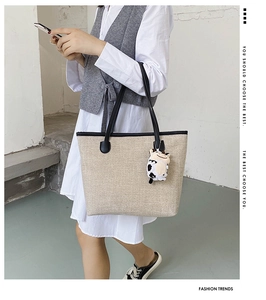 Detail of cream woven tote bag with black leather strap and cow plush pendant on model