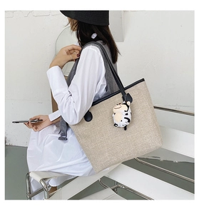 Detail of canvas tote bag with black leather trim and cute cow plush charm on handle