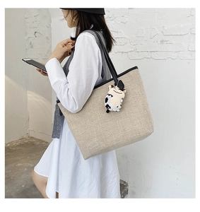 Detail of a beige canvas tote bag featuring black leather straps and a cute cow plush charm
