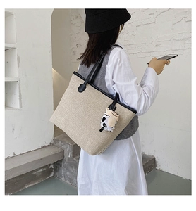 Detail of beige canvas tote bag with black leather straps and cow plush keychain
