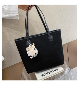 Detail of black canvas tote bag featuring a cute cow plush charm and slim handles