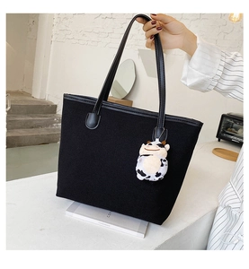 Detail of black canvas tote bag featuring leather handles and a plush cow charm decoration