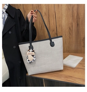 Detail of canvas tote bag featuring a cute plush cow pendant and leather shoulder straps