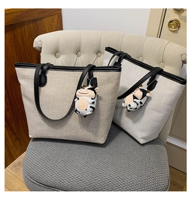 Detail of minimalist canvas tote bags with leather handles and decorative cow plush charms