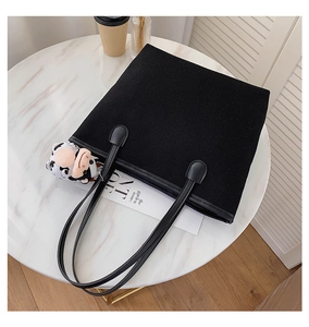 Detailed shot of a black canvas tote bag with a plush cow keychain on a marble table