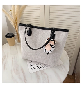 Close-up of cream canvas tote bag with black leather straps and cow plush pendant