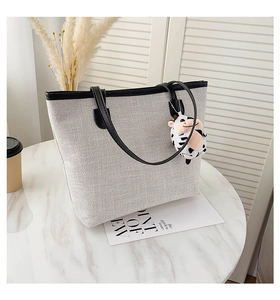 Detail of grey canvas tote bag with black trim and a cute cow plush pendant accessory