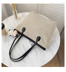 Detailed close-up of oatmeal canvas tote bag with black leather straps and cow plush charm