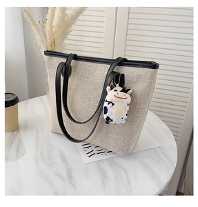 Detail of canvas tote bag with black leather straps and a cute cow plush pendant
