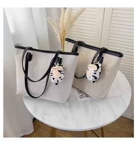 Detail of canvas tote bags with black faux leather handles and cute cow plush pendant
