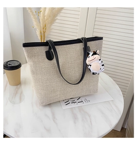 Close-up of beige canvas tote bag featuring black straps and a cute cow plush pendant