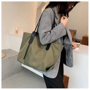 Close-up of olive green nylon tote bag featuring slim black leather straps for daily commute