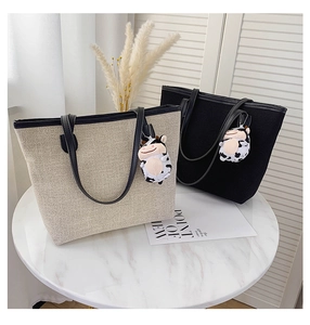 Macro detail of canvas tote bags in beige and black with leather straps and charms