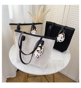 Detailed close-up of woven canvas tote bags in beige, black and grey with cow print charms