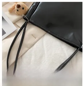 Detail of black PU leather tote bag featuring a cute brown plush bear charm and sleek straps