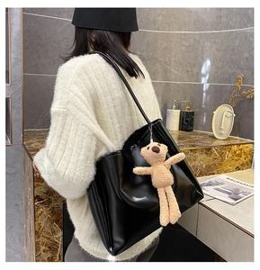 Detail of a large black tote bag with smooth glossy texture and a cute plush bear charm