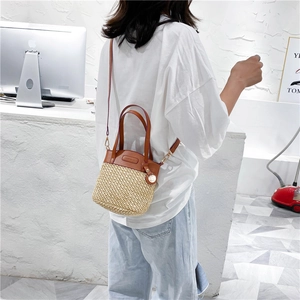 Handmade woven straw bucket bag with brown leather handles and adjustable shoulder strap