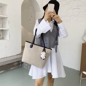 Large beige canvas tote bag with black leather straps and cute cow charm on a model