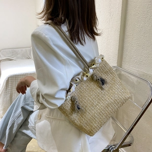 Beige straw tote bag with floral trim and tassels shown on model for summer fashion
