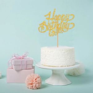 Close-up of golden glitter Happy Birthday cake topper on a white cake with soft pink decor