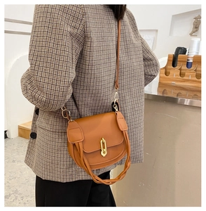 Dettaglio di una borsa a sella marrone con fibbia a U dorata e manico intrecciato