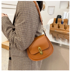 Borsa a sella marrone in pelle con fibbia a catena dorata su un blazer a quadri